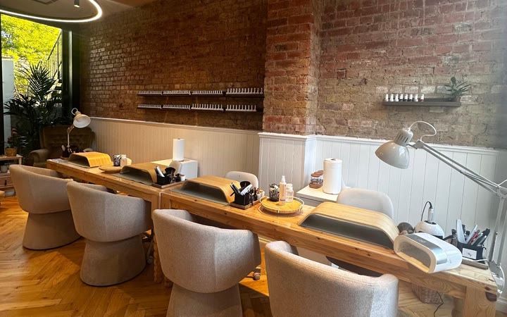 Manicure stations with lamps, polish and bouclé chairs along a white panelled wall
