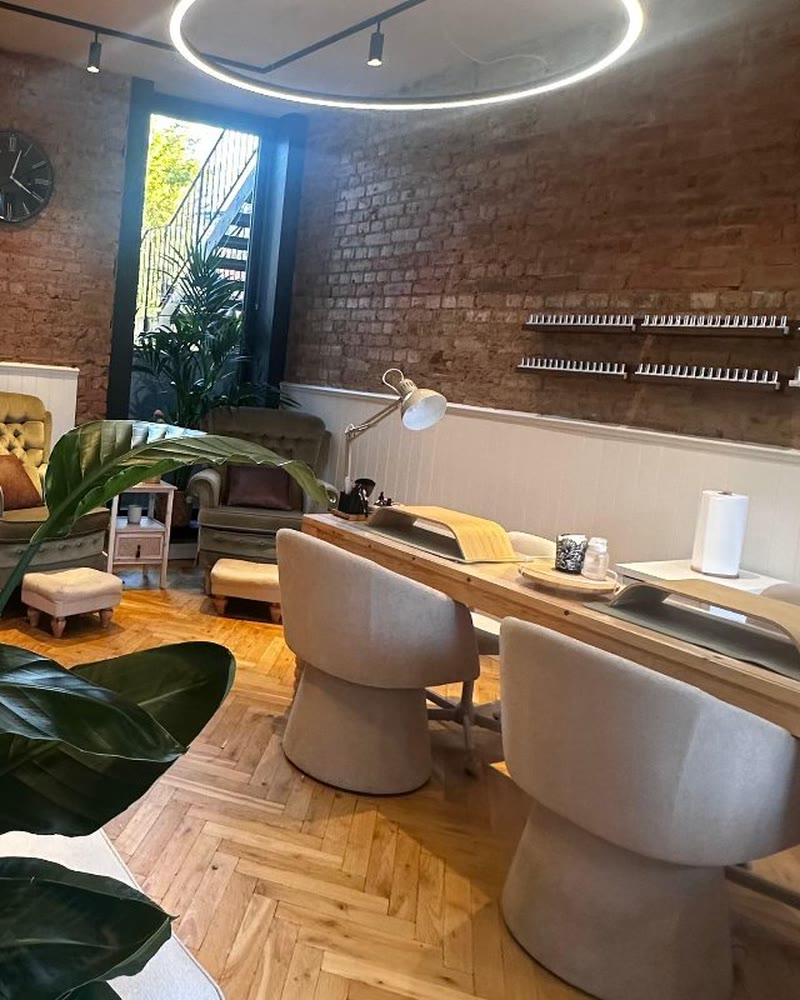 Inside Halo Nail Studio: exposed brick, a herringbone floor, cream bouclé chairs at a long oak nail bar and a ring light overhead